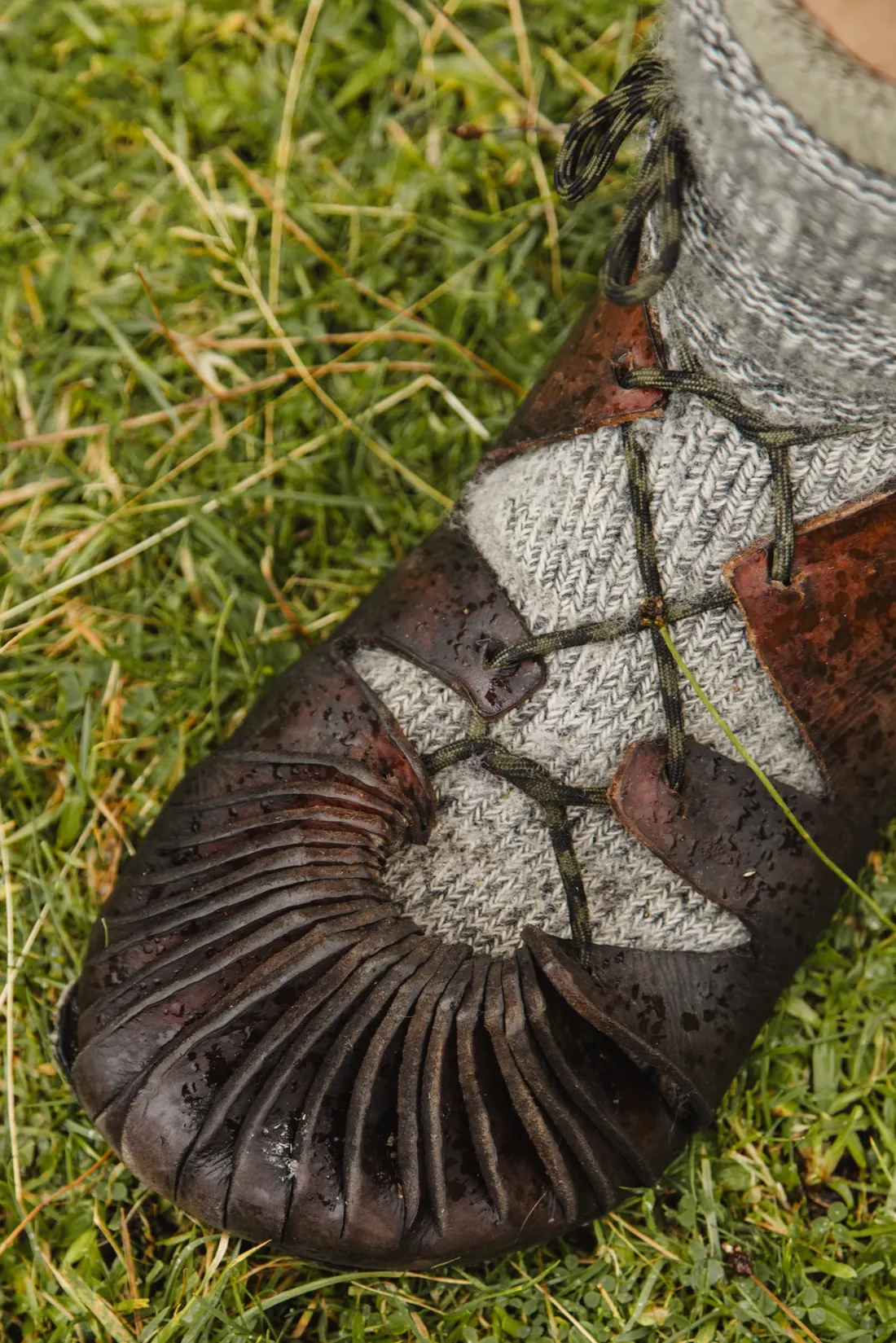A hand-stitched leather turnshoe laced over a wool sock, standing in grass
